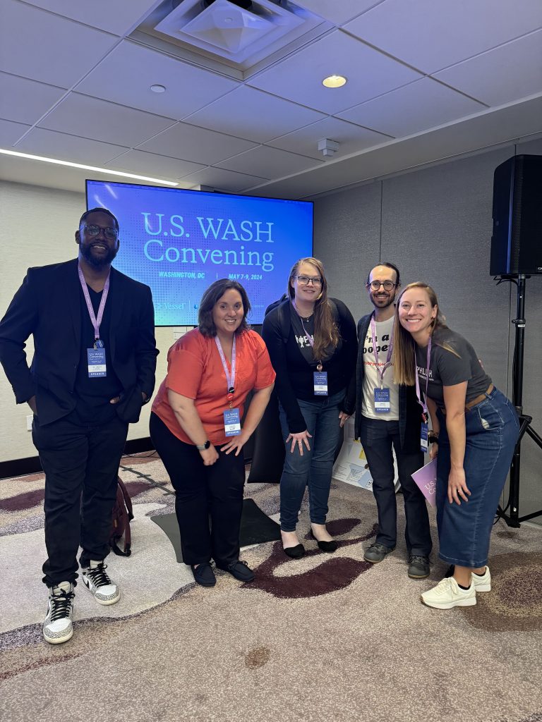 Five panelists pose in front of a screen displaying the words "U.S. WASH Convening"